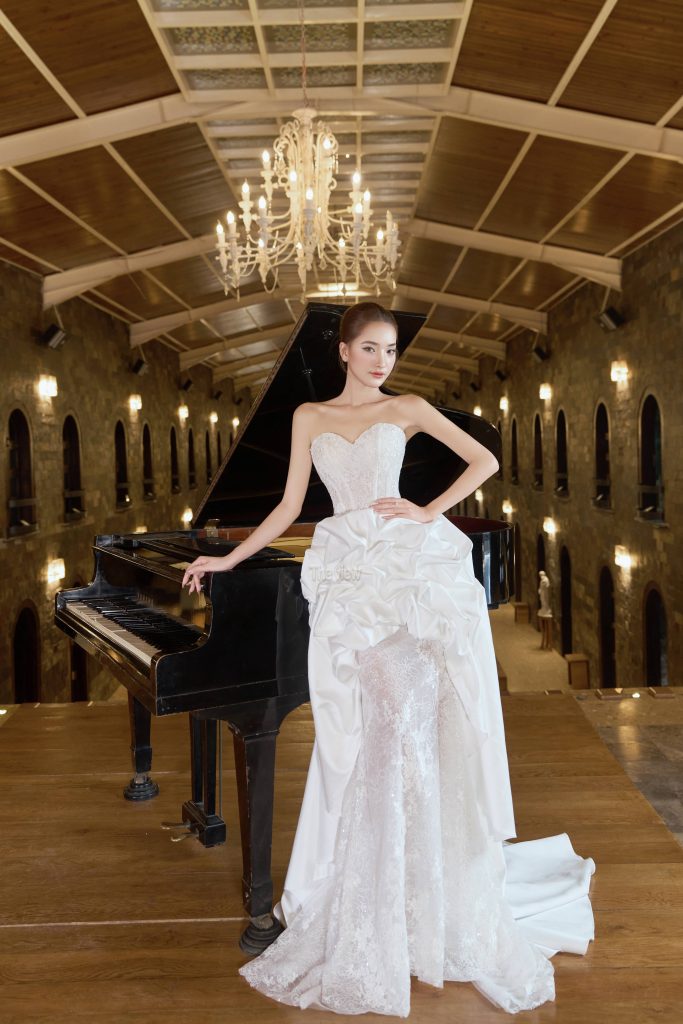 Váy cưới đuôi cá cúp ngực sang trọng với thiết kế độc đáo kết hợp phần nhún bồng xoè tạo điểm nhấn quyến rũ quanh hông, giúp khéo léo che khuyết điểm và tôn vinh vóc dáng. Thân váy đính ren dệt cao cấp lấp lánh tinh xảo, phom dáng corset ôm sát định hình eo thon, kết hợp tà sau thướt tha cùng bao tay ren đồng bộ, hoàn hảo cho cô dâu tỏa sáng trong đại lễ lẫn lúc đi bàn tiệc.
